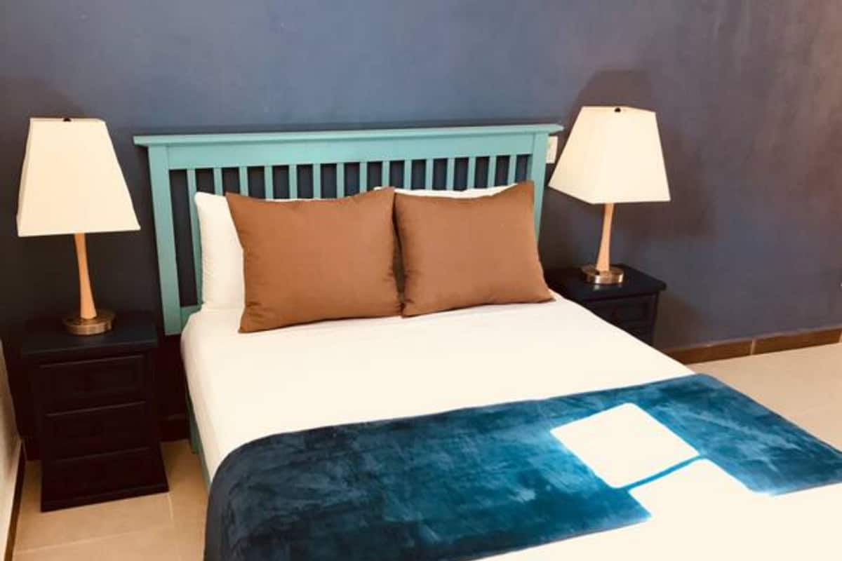 Ein Bett mit blauem Kopfteil, zwei Nachttischlampen und einer blauen Decke.
