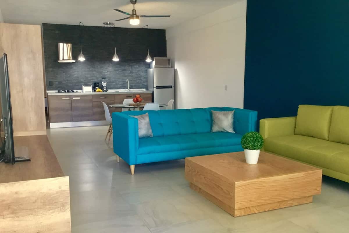 Ein modernes Wohnzimmer mit einem blauen Sofa, einem grünen Sofa und einem Holztisch.