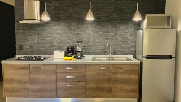 A modern kitchen with a dark backsplash, stainless steel appliances, and wooden cabinets.