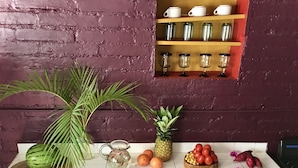A kitchen counter with a variety of fruits, a pitcher, and a small shelf with cups.