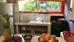 A kitchen with a sink, stove, and various fruits and vegetables on the counter.