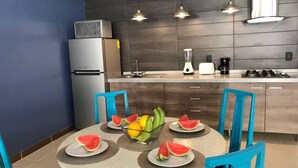 A modern kitchen with a round dining table, blue chairs, and a fruit centerpiece.