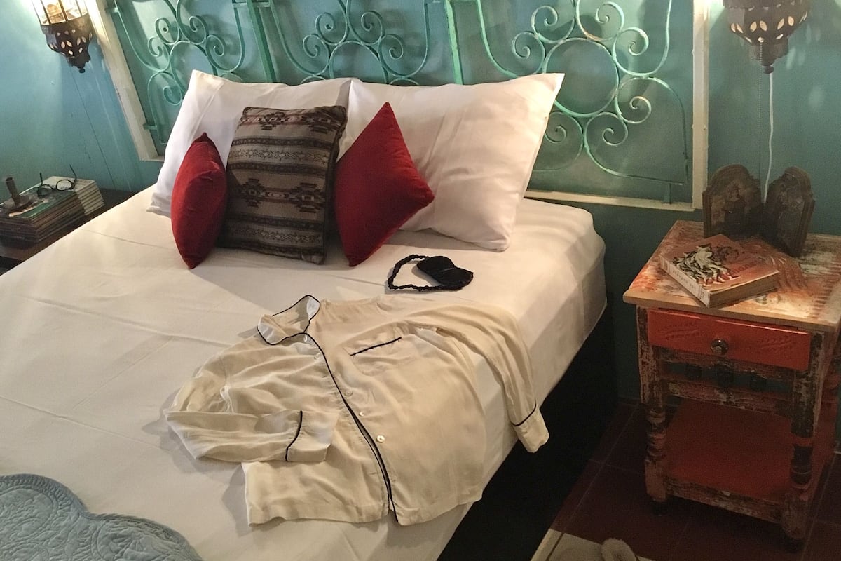 Ein ordentlich bezogenes Bett mit Kissen, ein Nachttisch mit einem Buch und einer Lampe.