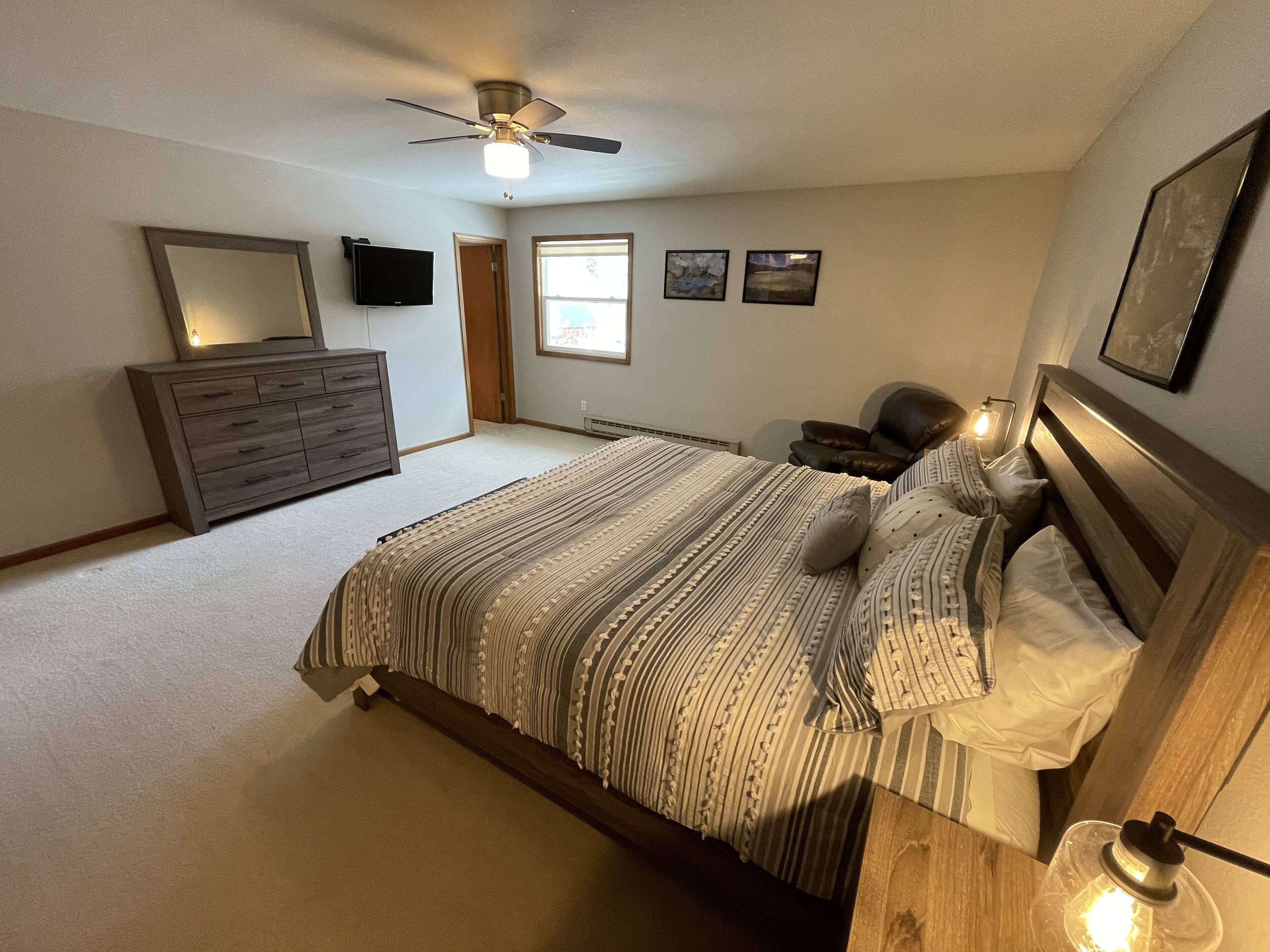 A bedroom with a bed, a dresser, a ceiling fan, and a window.