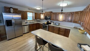 Una cocina moderna con armarios de madera, electrodomésticos de acero inoxidable, una isla central con taburetes altos y luces colgantes.