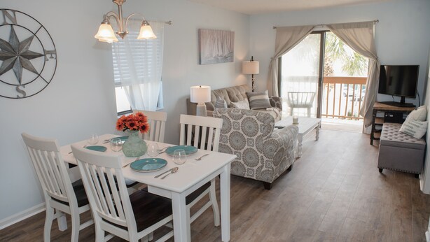 A dining area with a white table and chairs, a chandelier, and a dining set. - Beautiful Condo steps away from Beach (St. Augustine Beach)