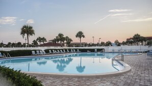A swimming pool with lounge chairs, palm trees, and a white fence. - Beautiful Condo steps away from Beach (St. Augustine Beach)