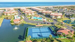 An aerial view of a coastal resort with multiple buildings, a swimming pool, tennis courts, and a marina. - Beautiful Condo steps away from Beach (St. Augustine Beach)