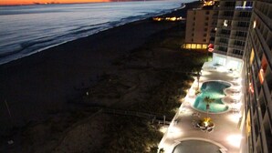 Zona de piscina en la azotea con varias piscinas, sillas de descanso y vista a la playa y al océano al atardecer.