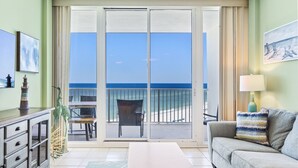 Una habitación con balcón, sofá, mesa y sillón.