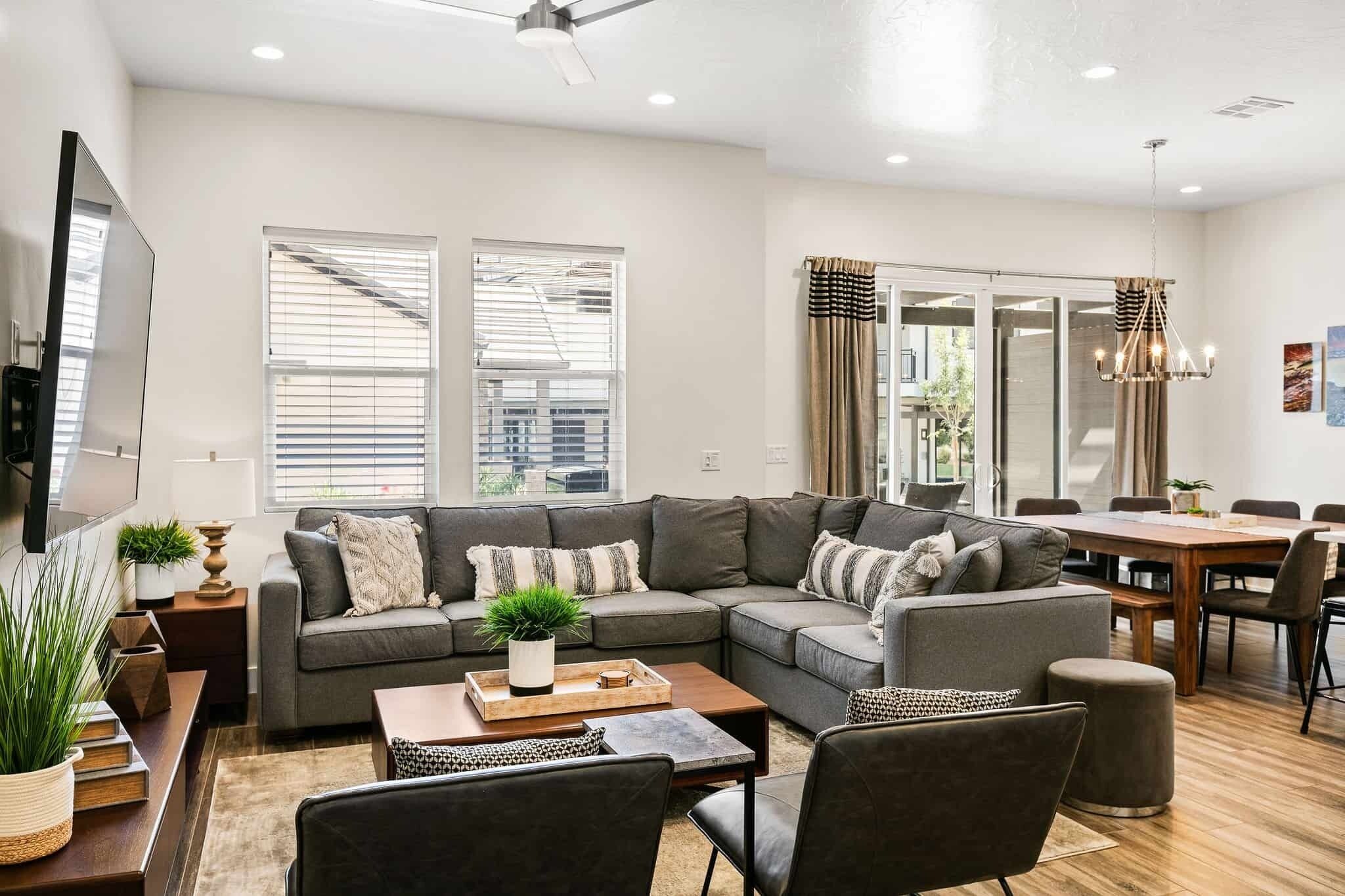 A modern living room with a sectional sofa, a dining table, and a TV mounted on the wall.