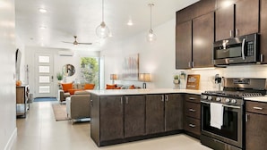 A modern kitchen with dark cabinets, stainless steel appliances, and pendant lighting.