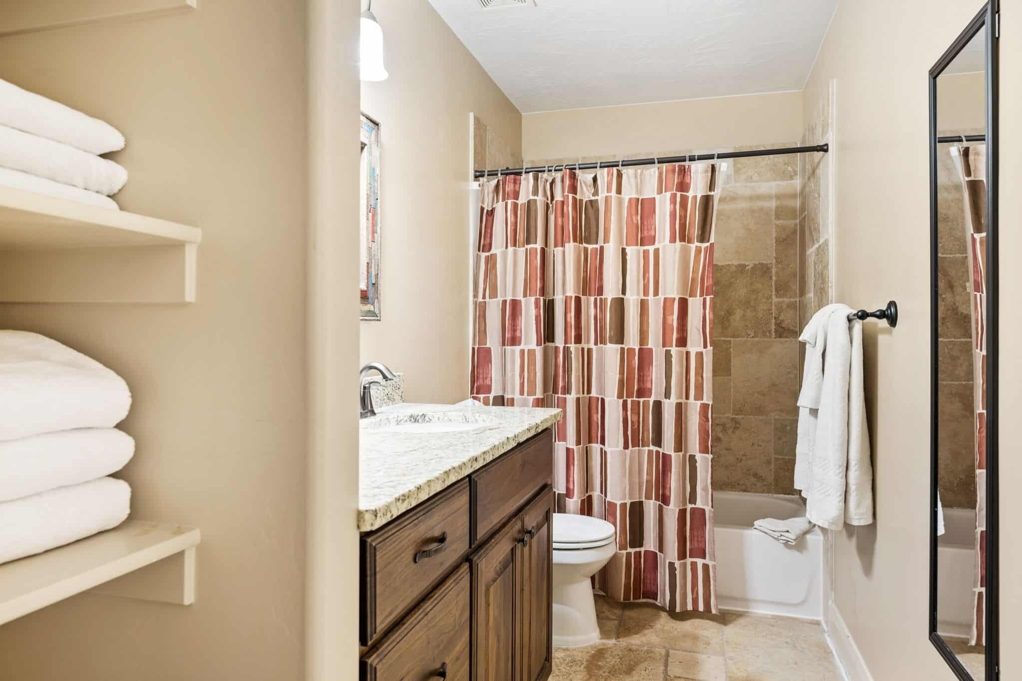 A bathroom with a shower curtain, a toilet, and a sink with a mirror.