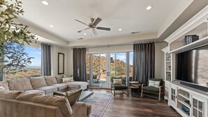 A spacious living room with a sectional sofa, a TV cabinet, and a view of a desert landscape through large sliding glass doors. - Sunset on the 5th 3 Bedroom Townhouse by RedAwning (Washington)