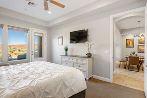 A bedroom with a large bed, a dresser, a TV, and a view of the desert through the window. - Views Over Coral Canyon by RedAwning (Washington)