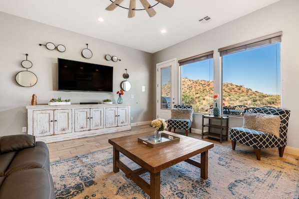 A living room with a large TV, white cabinets, a wooden coffee table, and a view of a desert landscape through large windows. - Views Over Coral Canyon by RedAwning (Washington)