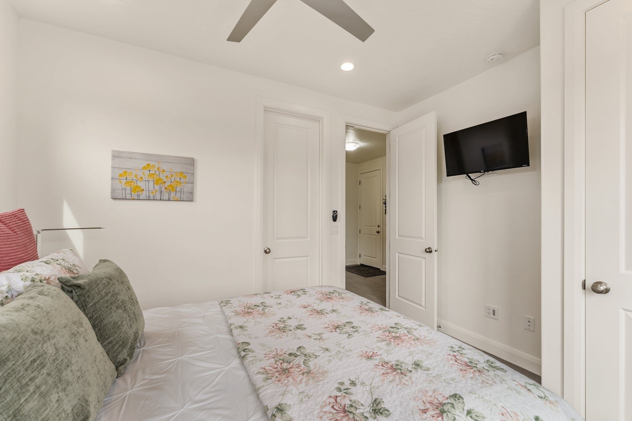 A bedroom with a bed, a painting, a television, and a door leading to another room.