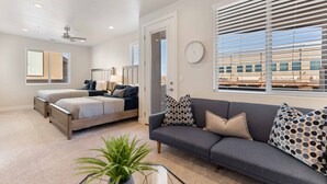 Ein modernes Wohnzimmer mit einer Couch, zwei Betten, einem Deckenventilator und großen Fenstern mit Jalousien.