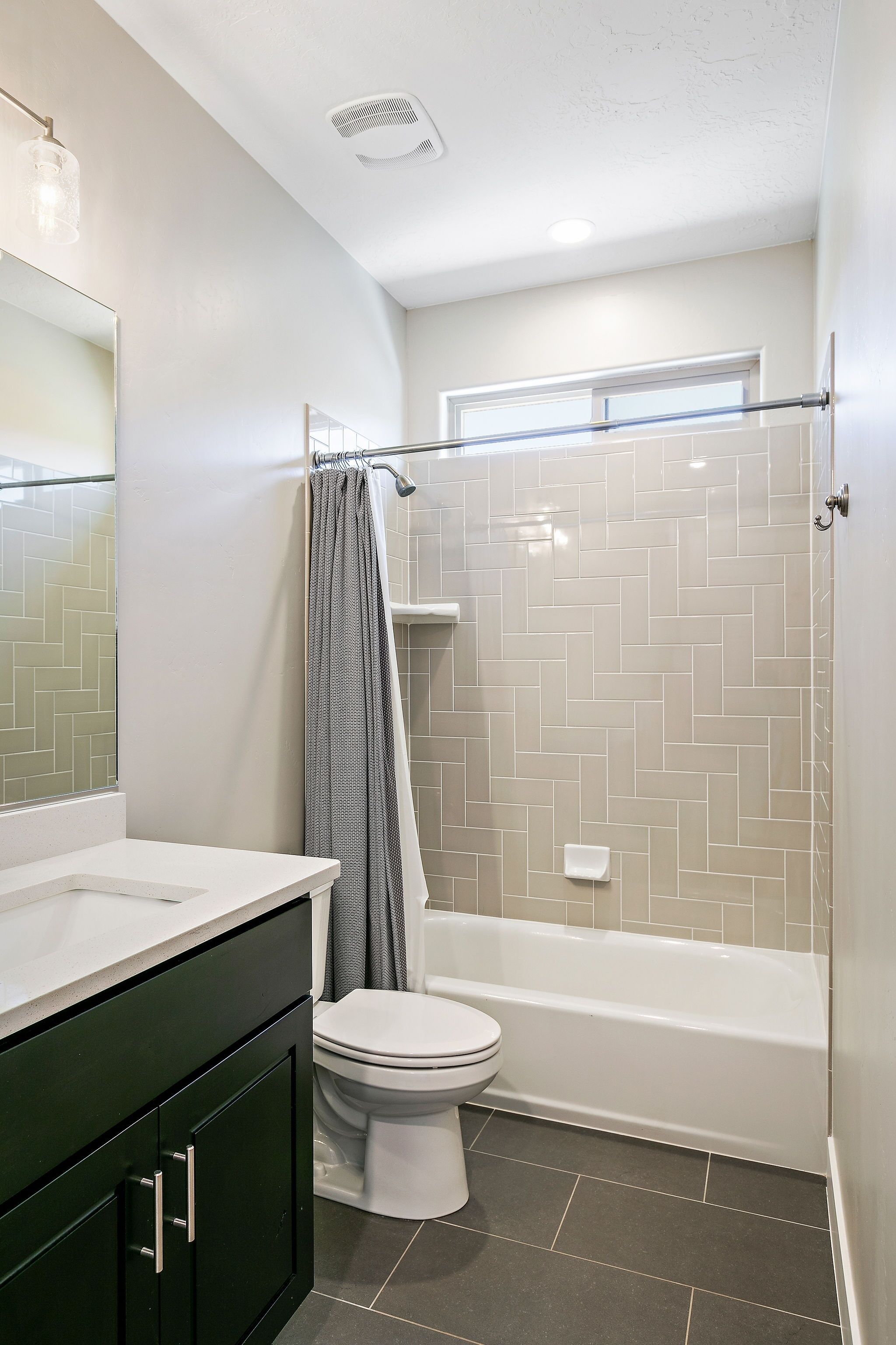 A modern bathroom with a white toilet, a bathtub, and a shower area with a herringbone tile pattern.
