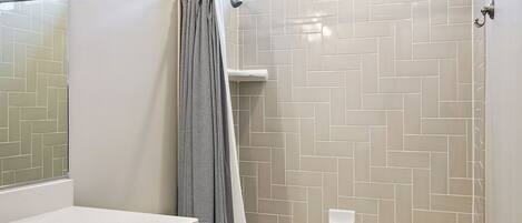 A modern bathroom with a white toilet, a bathtub, and a shower area with a herringbone tile pattern.