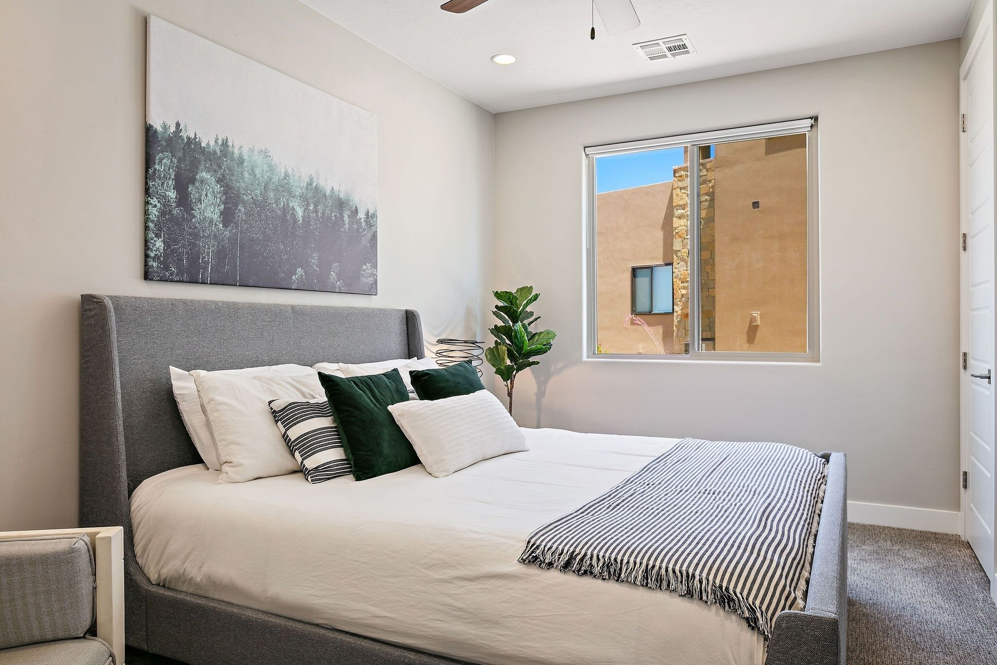 Ein Schlafzimmer mit einem großen Bett, Blick auf ein Gebäude durch ein Fenster und einem Bild an der Wand.