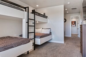 Habitación pequeña con literas, una escalera, un reloj y una puerta que da a otra habitación.