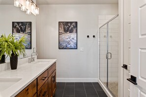 Un baño moderno con tocador blanco, ducha con puertas de vidrio y dos cuadros en la pared.