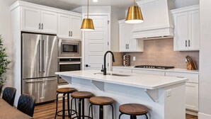 A modern kitchen with white cabinetry, stainless steel appliances, and a central island with stools.