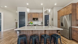 A modern kitchen with a large island, wooden cabinets, stainless steel appliances, and bar stools. - Ocotillo Springs #20 by RedAwning (Santa Clara)