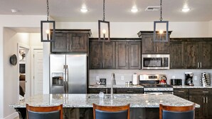 Una cocina con armarios de madera oscura, una isla de granito con taburetes de bar, electrodomésticos de acero inoxidable e iluminación colgante.