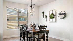 Comedor con mesa y sillas de madera, candelabro y decoración en la pared, incluyendo un arreglo floral y espejos.
