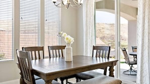 A dining area with a wooden table, six chairs, a vase with flowers, and a chandelier.