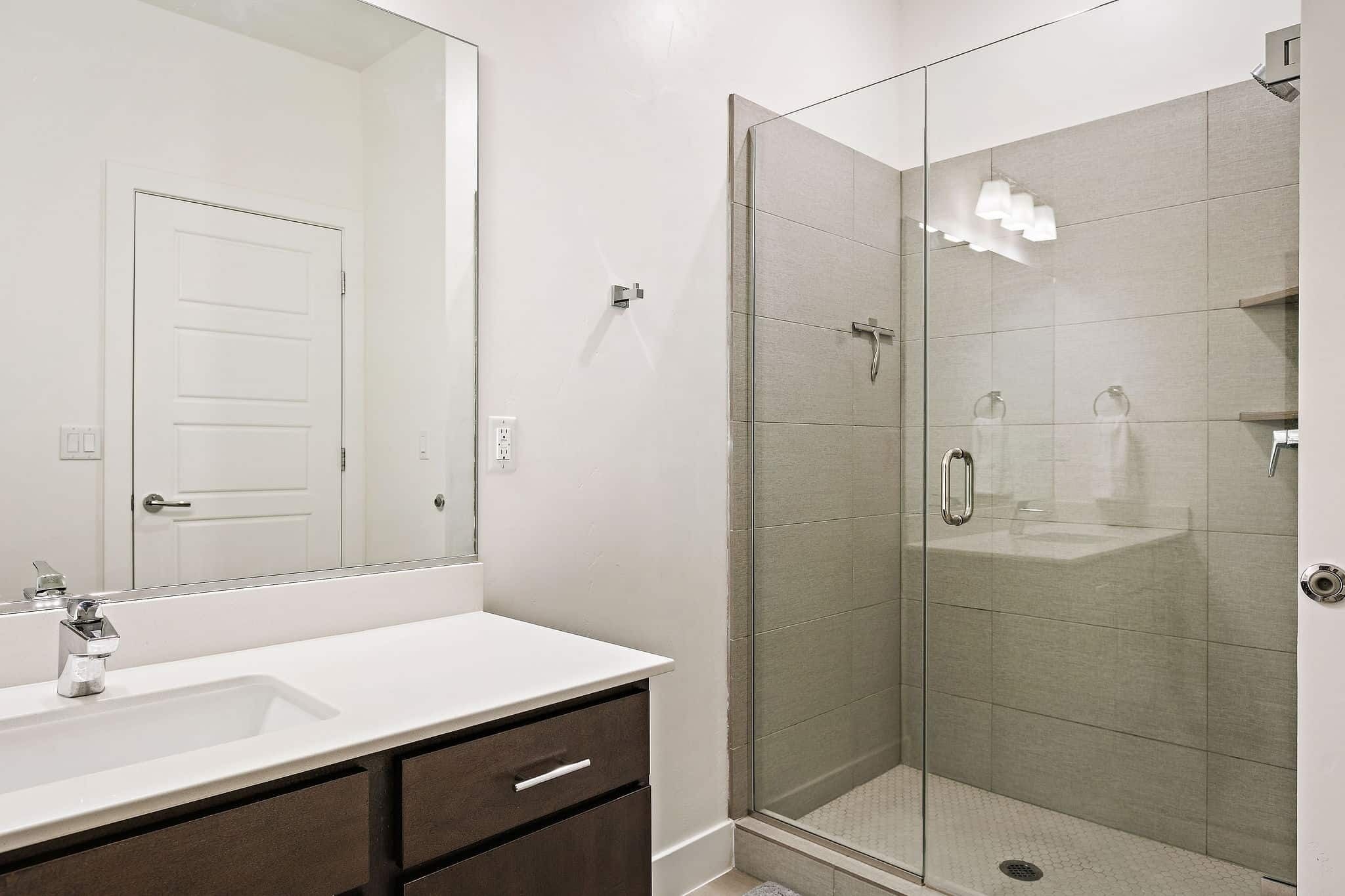 A modern bathroom with a glass-enclosed shower, a white sink with a mirror, and a door.