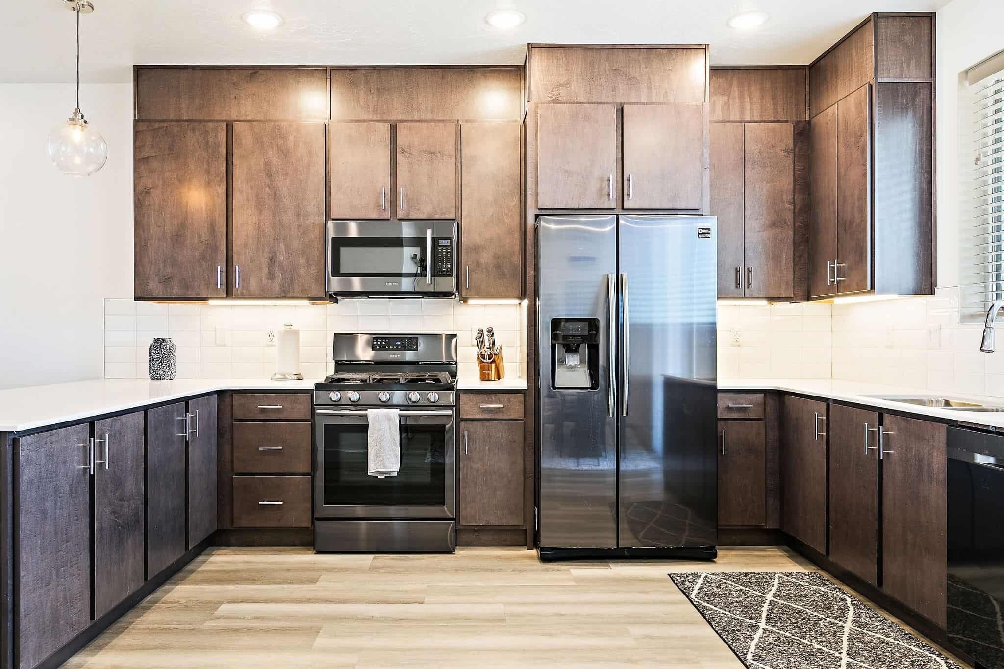 A modern kitchen with dark wooden cabinets, stainless steel appliances, and a light-colored countertop.