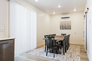 A dining area with a wooden table and chairs, a patterned rug, and an air conditioning unit on the wall. - Sunrise Corner by RedAwning (St. George)