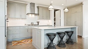 A modern kitchen with light grey cabinets, a white island with bar stools, and pendant lighting. - Enchanting Encanto #1 by RedAwning (Ivins)
