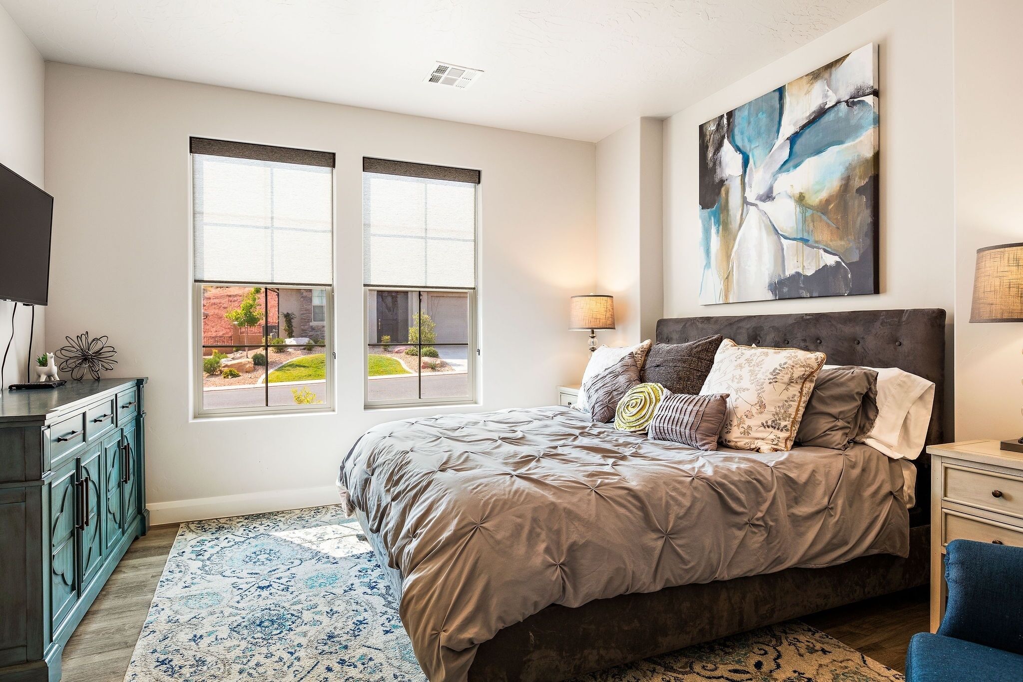 A bedroom with a large bed, a nightstand, a dresser, and a window with a view of the outside.