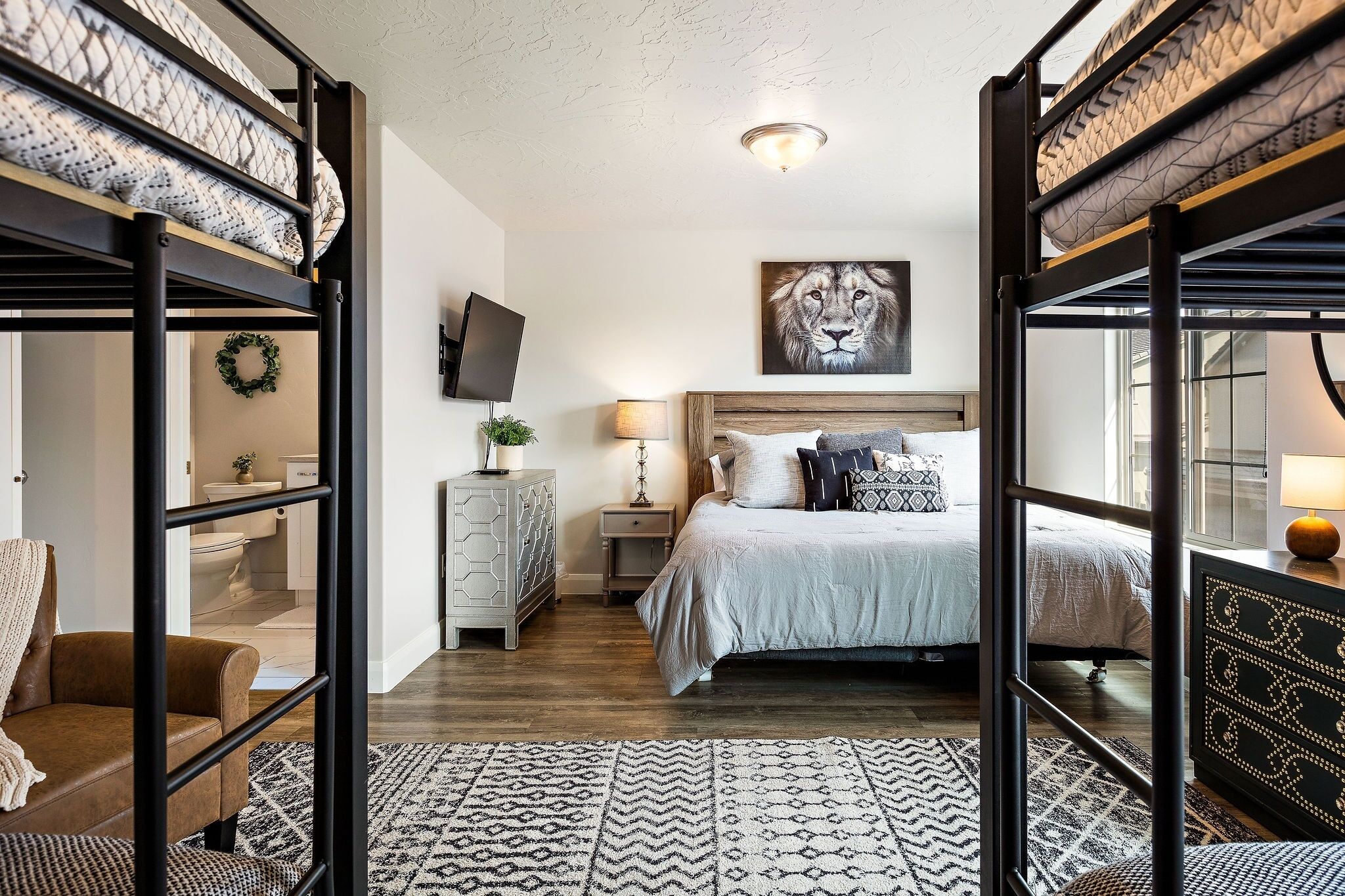 A bedroom with a bunk bed, a television, a framed artwork, a bedside table, and a patterned rug.