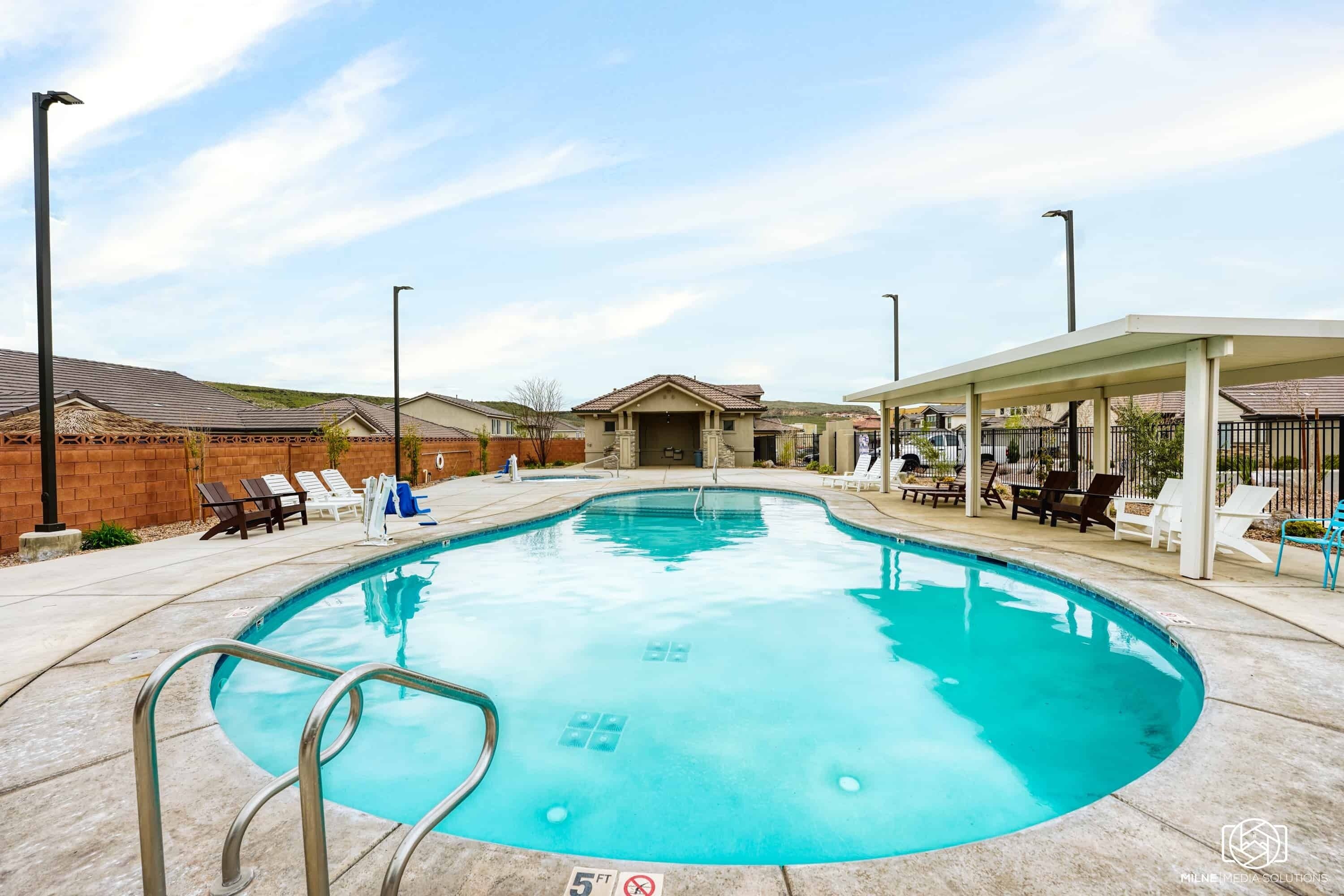 A swimming pool with a 5 ft depth limit sign, surrounded by lounge chairs and a covered seating area.