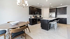 A modern kitchen with dark cabinetry, a central island, and a dining area with a round table and chairs.