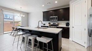 A modern kitchen with dark cabinets, stainless steel appliances, a large island with bar stools, and a sliding glass door to the outside.