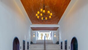 A spacious interior with a staircase leading to an upper level, a wooden ceiling, and a modern chandelier.