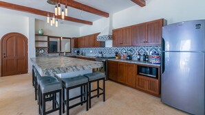 A kitchen with a marble island, wooden cabinets, a stainless steel refrigerator, and a hanging light fixture.
