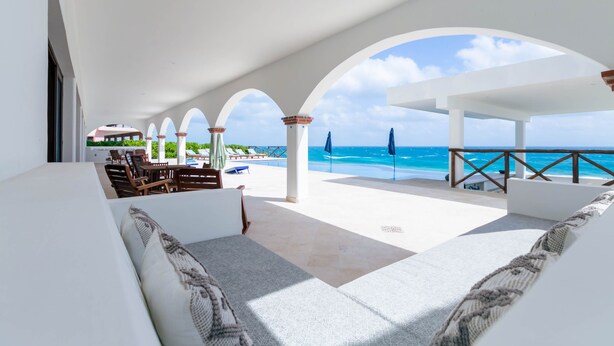 A spacious outdoor lounge area with a view of the ocean, featuring a seating area with sofas and a dining setup.