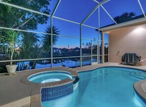 Ein überdachter Schwimmbereich mit Glasfassade, einem Whirlpool und Blick auf ein Gewässer und eine entfernte Landschaft.
