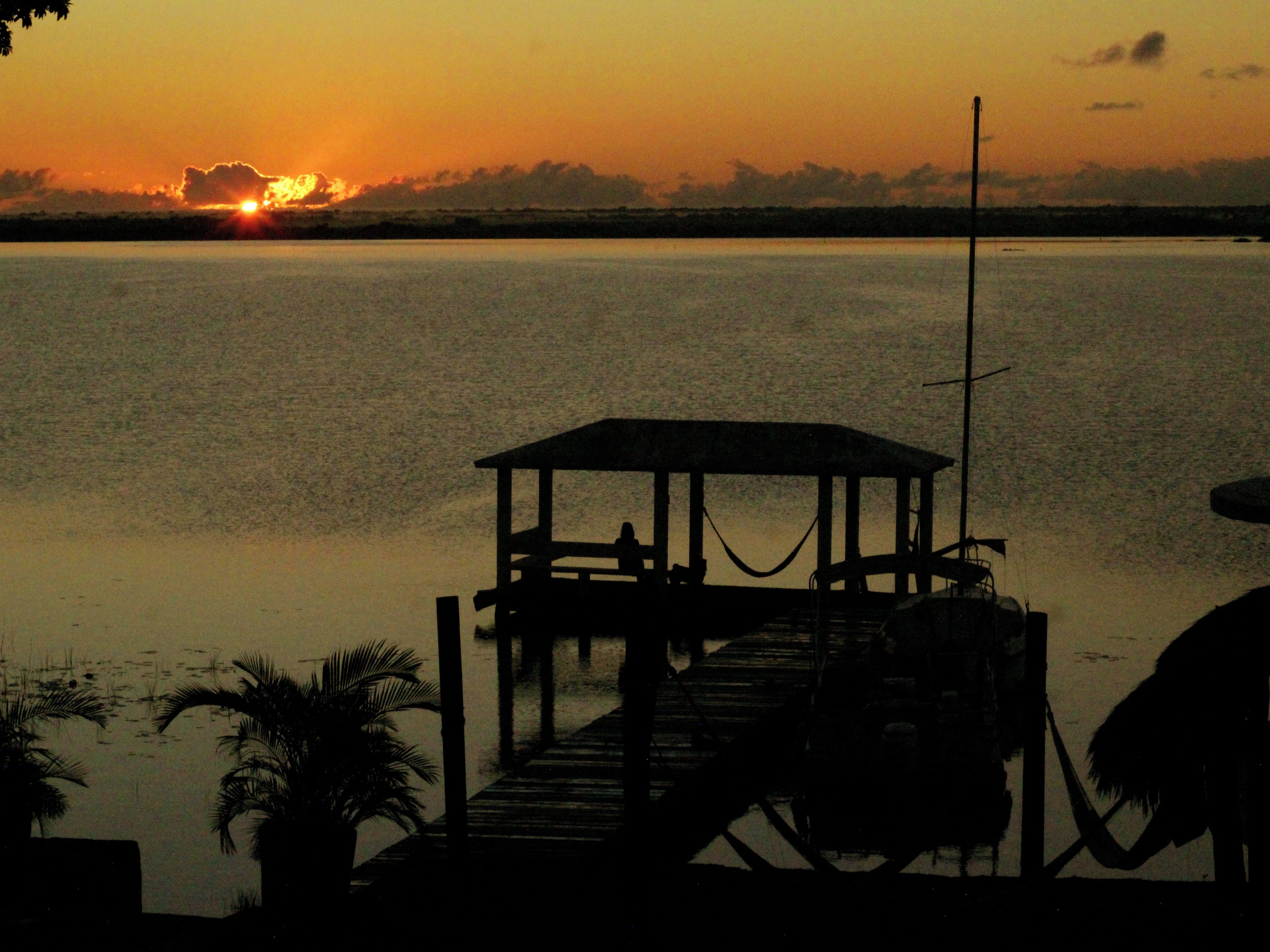 A dock extending into calm water with a sunset in the background.