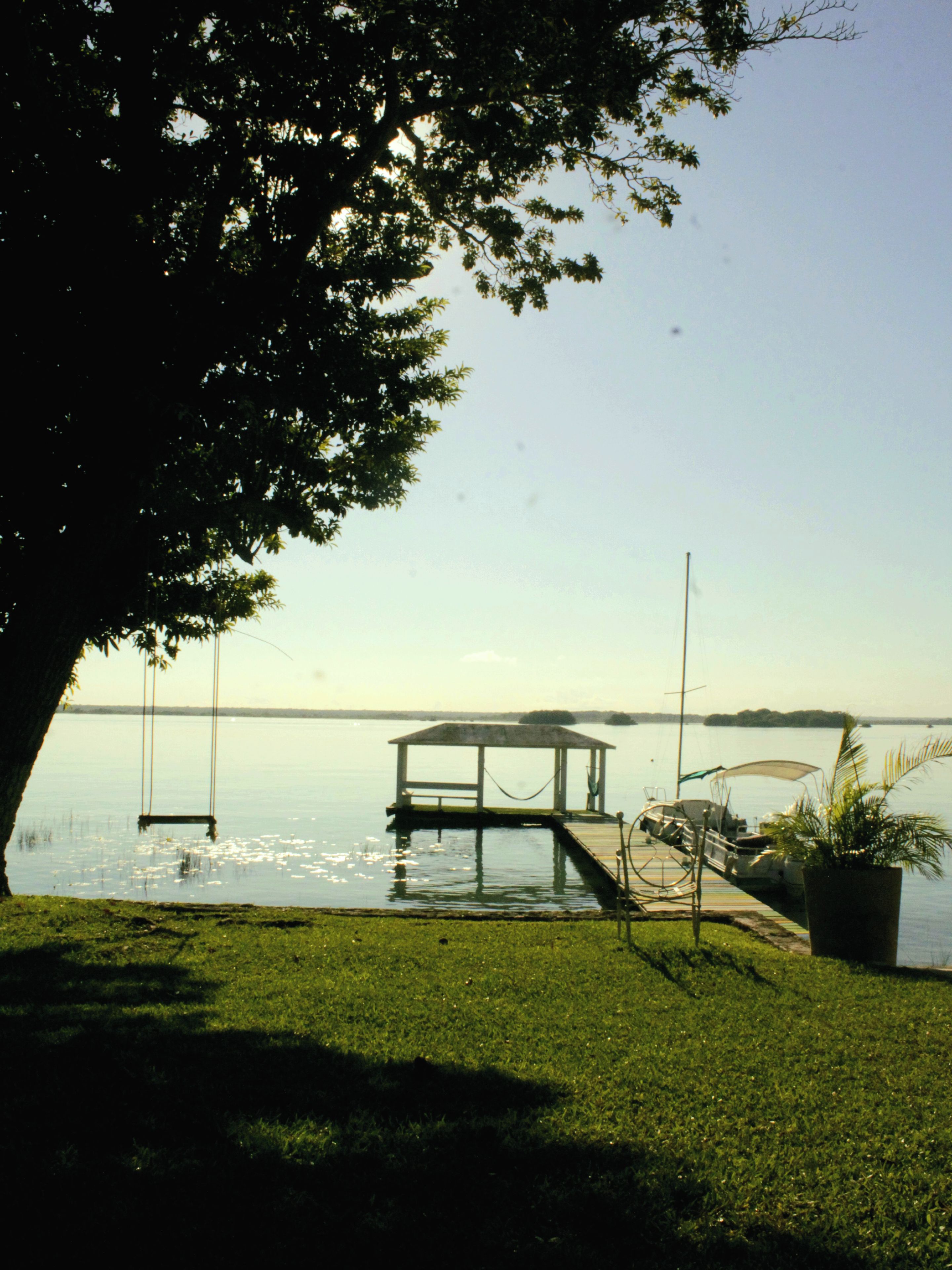 A dock extending into calm water, a gazebo, and a grassy area with a tree providing shade.