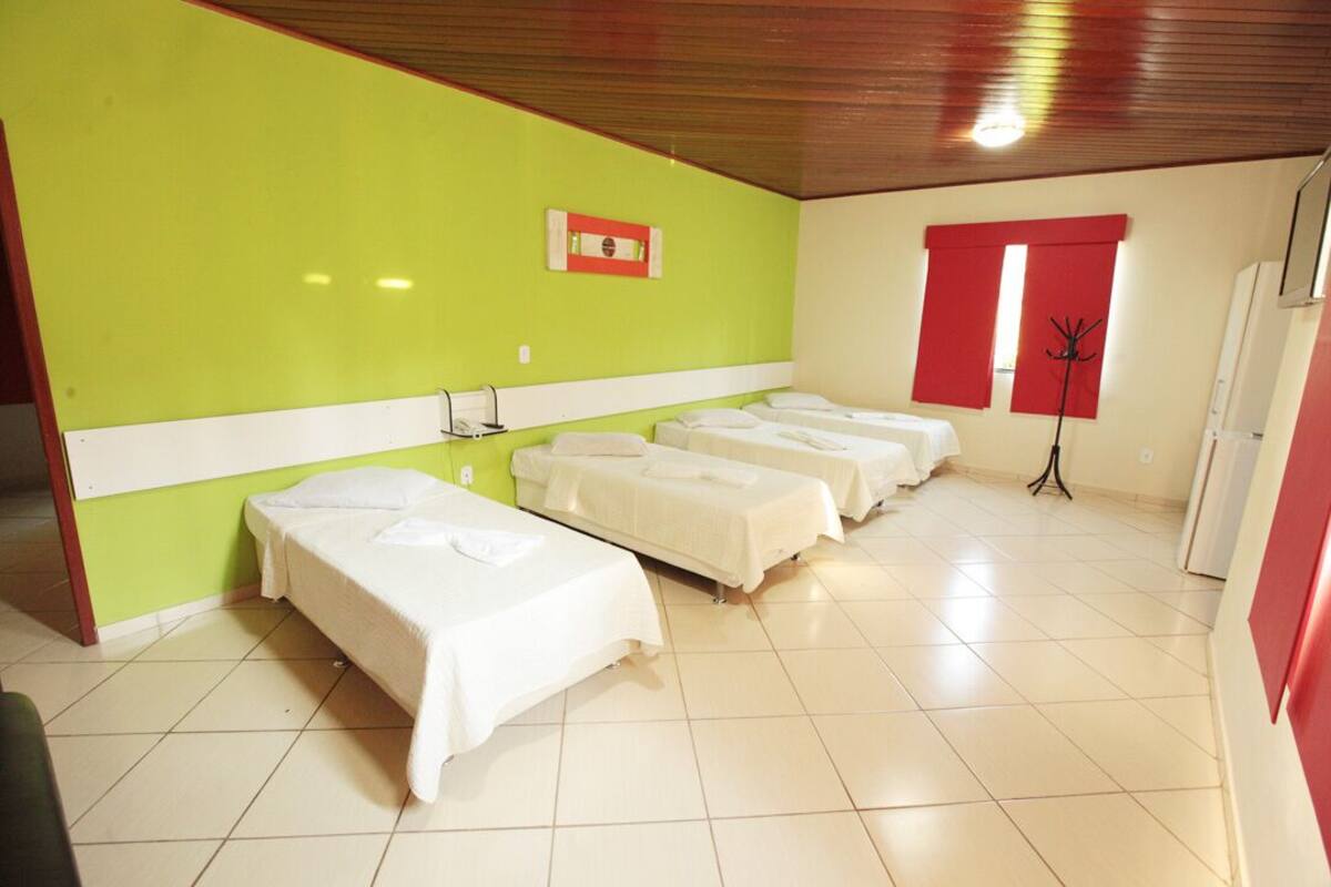 Habitación de hotel con cuatro camas dispuestas en fila, una ventana roja y un perchero.