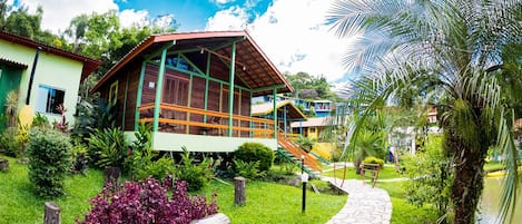 A building with a green roof and wooden exterior, surrounded by lush greenery and a stone pathway.