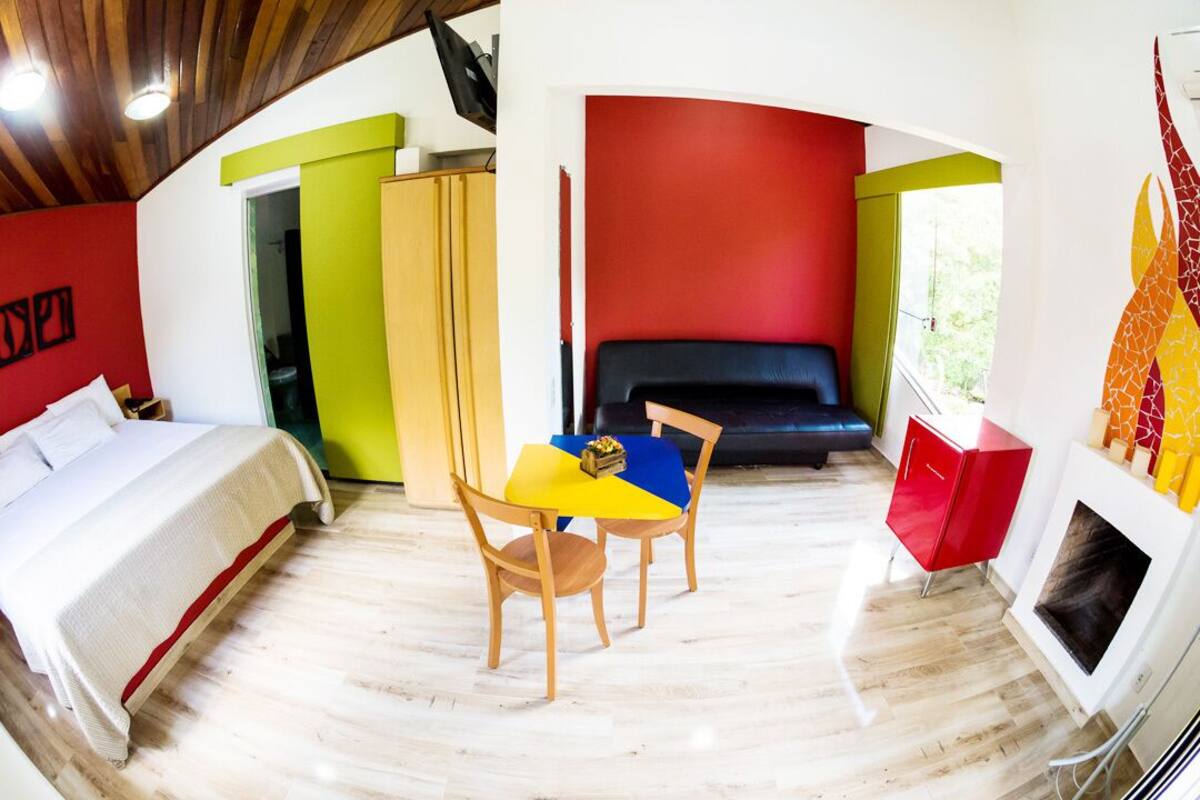 Una habitación con una cama, una mesa con sillas, un armario rojo y una chimenea.